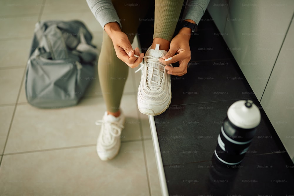 Primer plano de una atleta atándose los cordones de sus zapatillas en el vestuario del gimnasio.