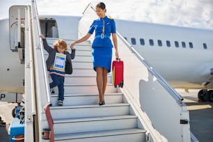 Cabin attendant wearing a blue outfit helping a small boy with an identity form in getting off the plane