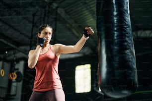 Young female athlete punching boxing bag during cross training in health club.