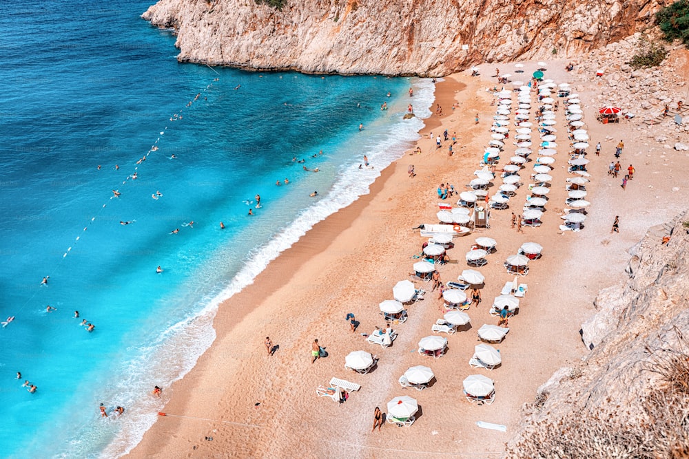 A chic beach with sun loungers and bathing vacationers. Top view of white sand and rich azure water