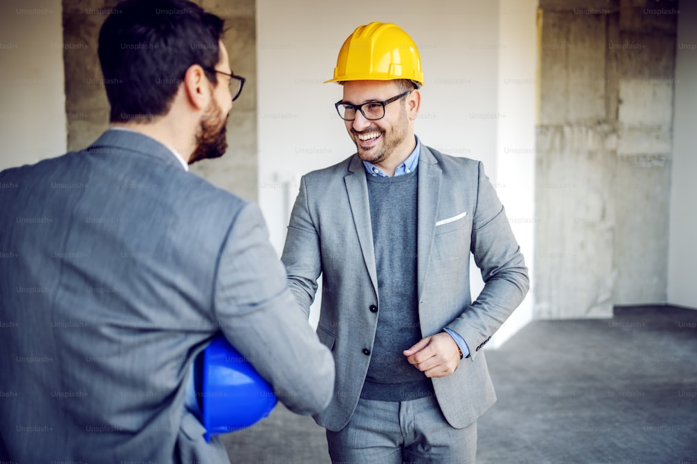 Handsome caucasian friendly real estate agent introducing himself to investor. Building in construction process interior.