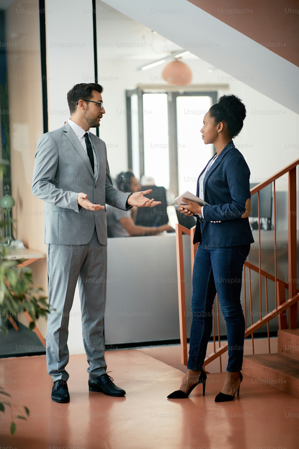 Businessman and his African American female coworker talking in a hallway.