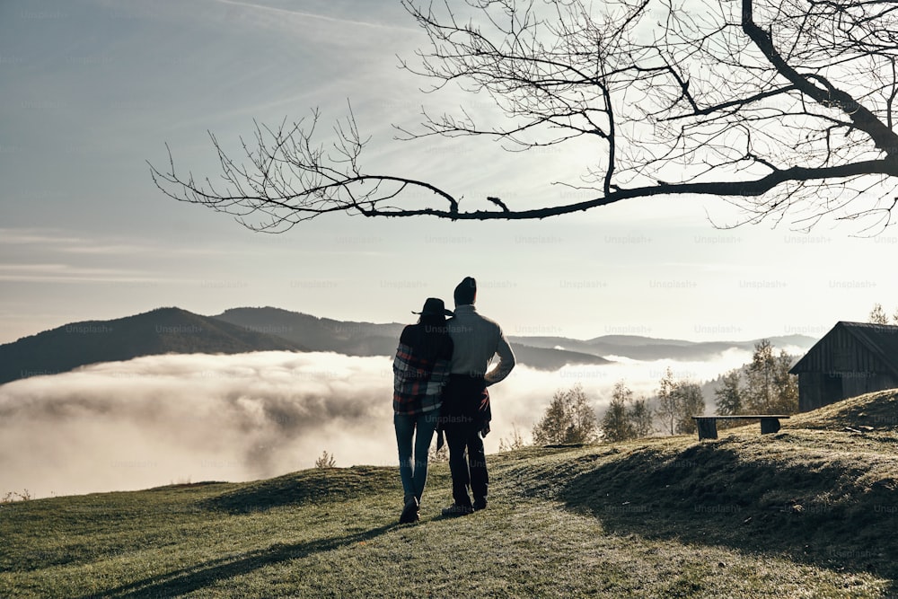Rückansicht des jungen Paares, das sich umarmt und den perfekten Blick auf die Bergkette genießt