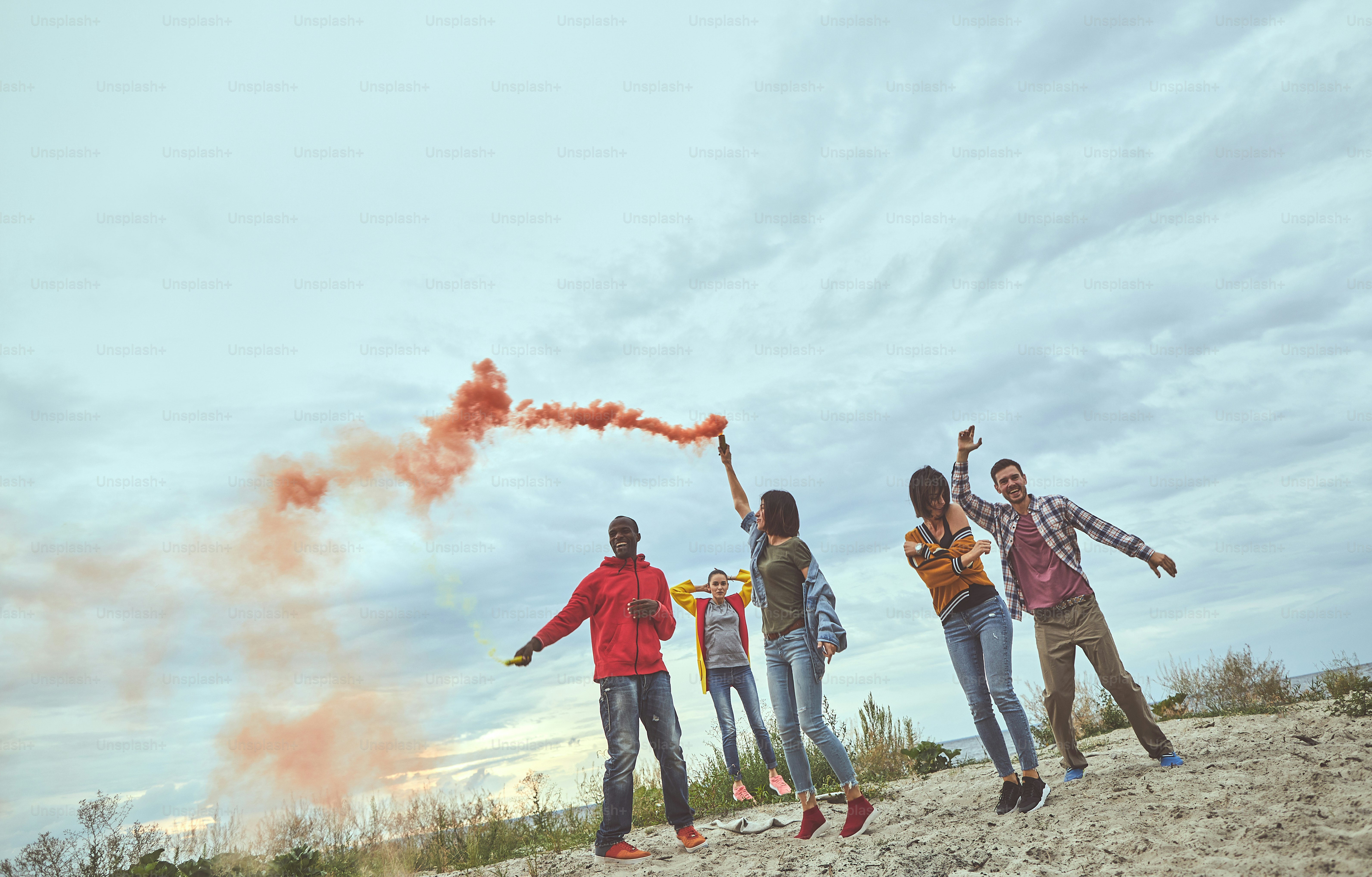 C’est l’heure de la danse. Portrait en pied d’hommes et de femmes se sentant heureux et dansant avec des fusées éclairantes sur la plage de la mer