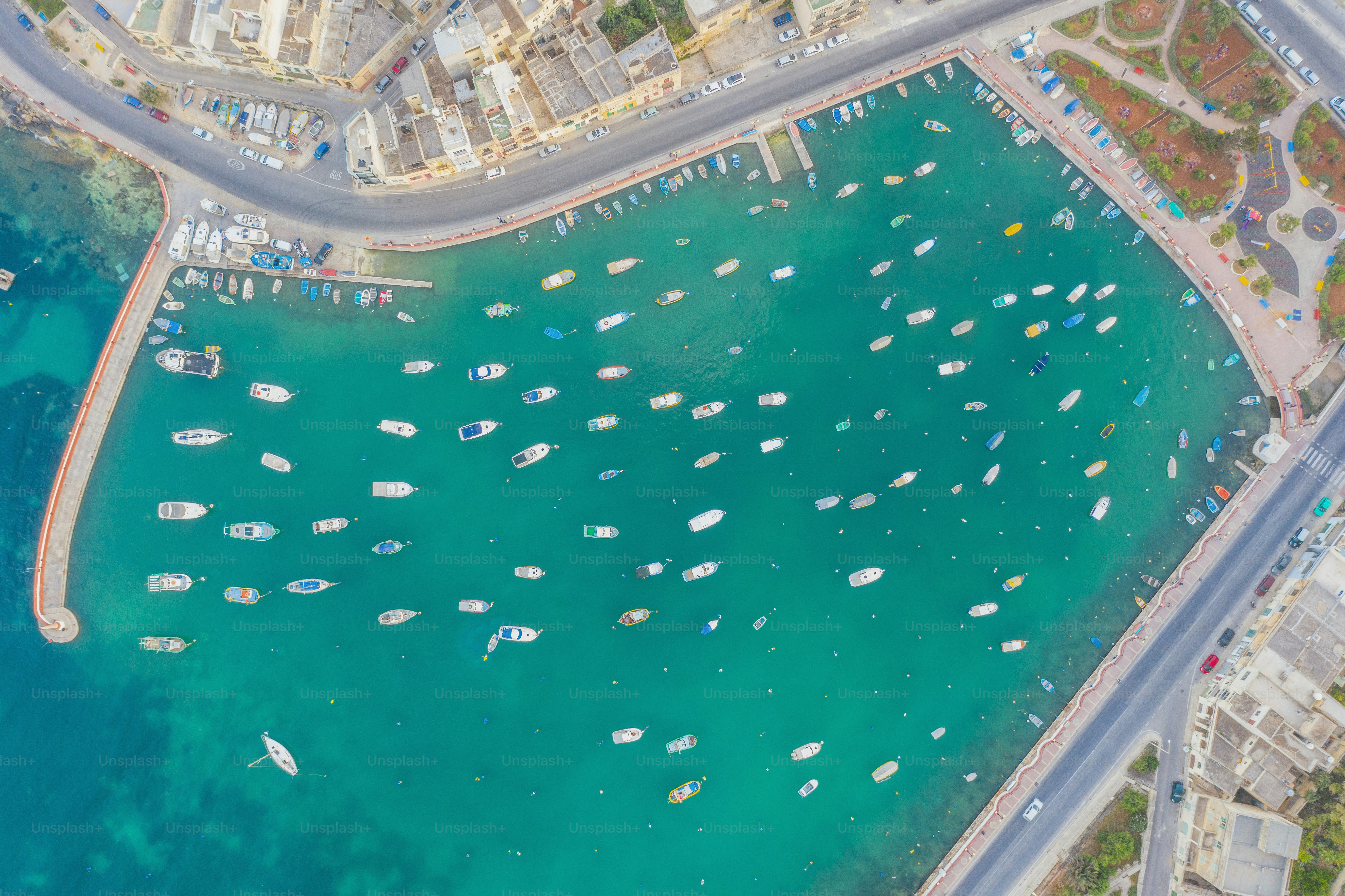 Piccole barche con vista aerea dall'alto nella baia acqua azzurra, baia della città, porto turistico e passeggiata con strada e case