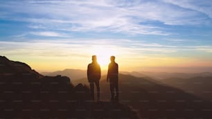The couple standing on the mountain on the beautiful sunrise background