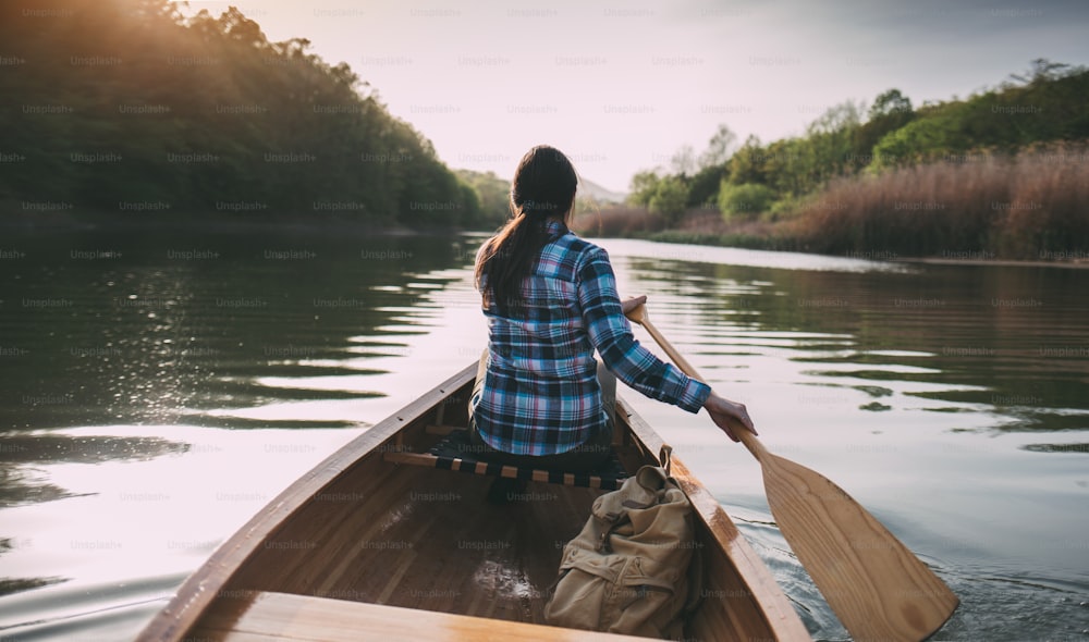 Rear view of hipster girl paddling the canoe on the sunset lake.