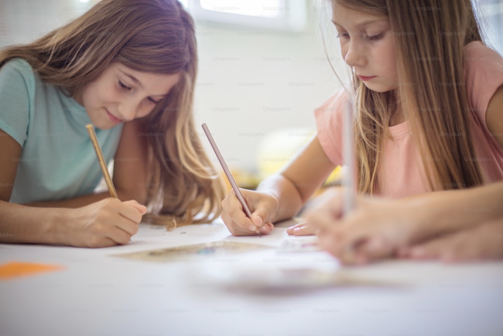함께 시험을 치르는 두 소녀. 십대 학생들은 교실에 앉아 글을 쓰고 있습니다. 초점은 배경에 있습니다.