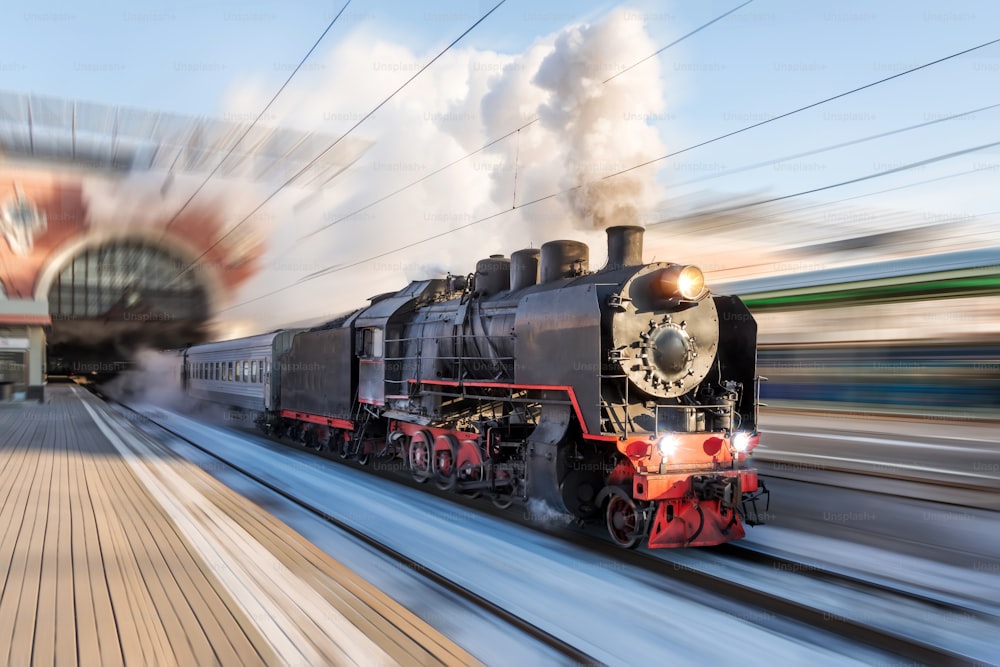 El vapor de la locomotora con poderosas nubes de humo sale de la estación para una velocidad de movimiento de viaje retro