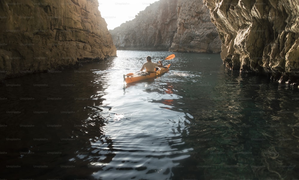 Vue arrière d’un homme pagayant en kayak dans une grotte. Kayak et spéléologie en même temps.