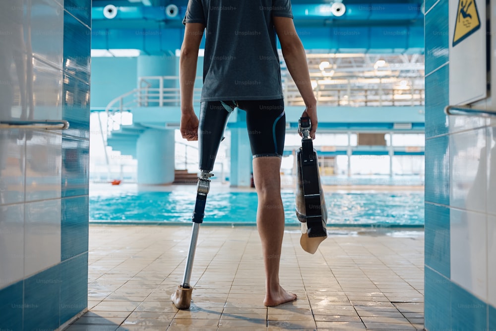 Back view of unrecognizable adaptive swimmer standing in front of indoor swimming pool.