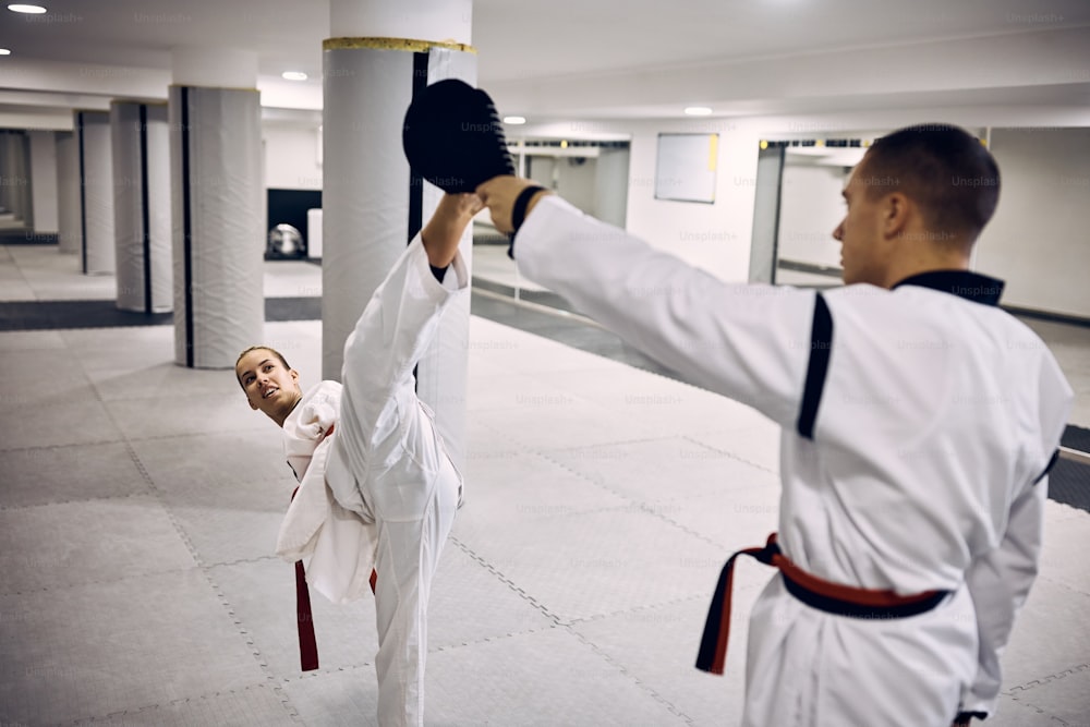 Martial artist with para-ability exercising high kick with her sparing partner while practicing taekwondo in health club.