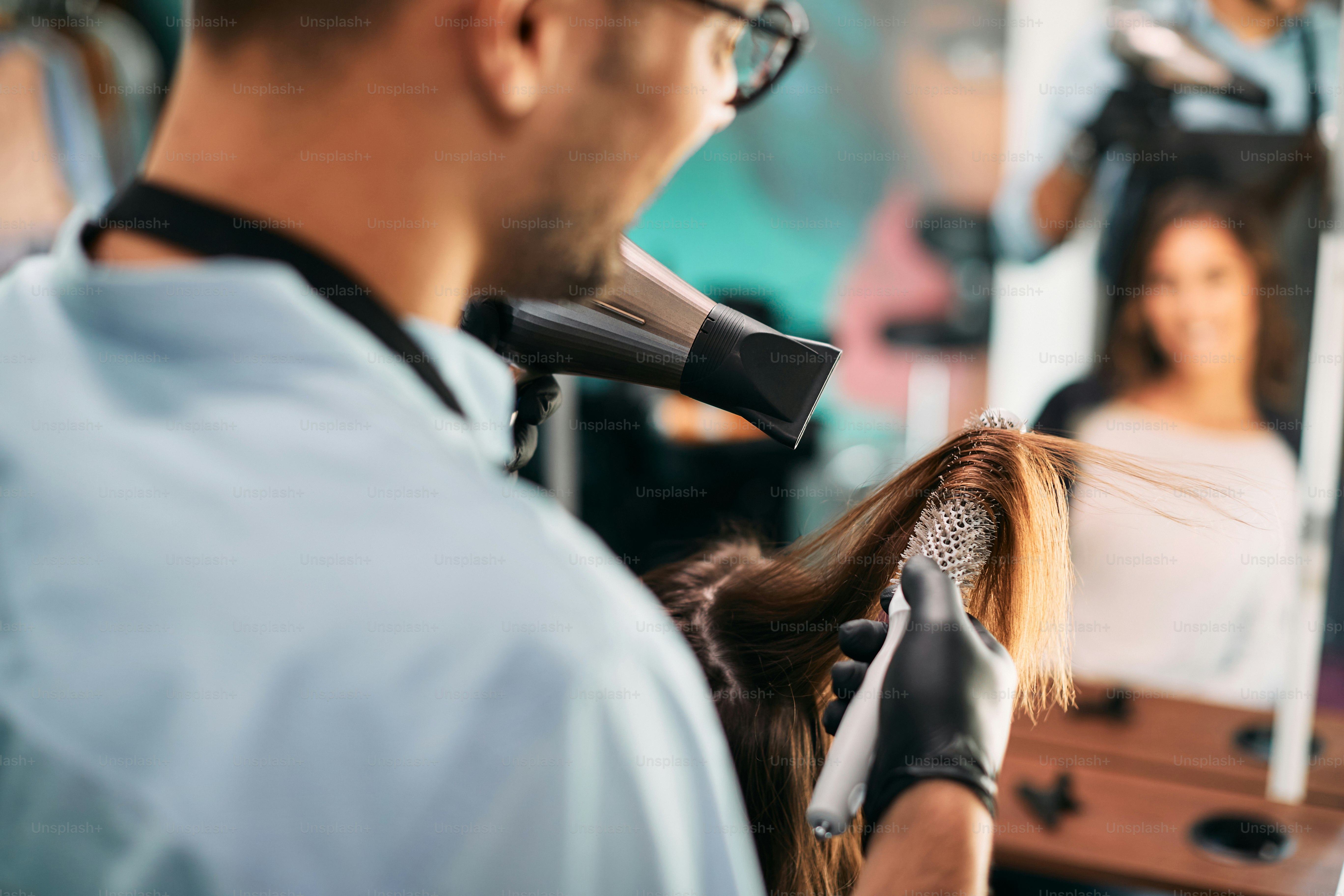 Nahaufnahme des Friseurs mit Fön und runder Bürste beim Styling der Haare des Kunden im Salon.