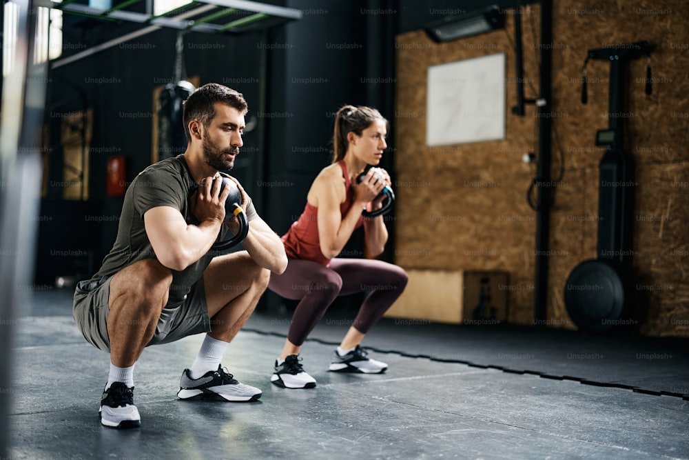 Junge Athleten, die Kettlebells verwenden, während sie Kniebeugen während des Sporttrainings im Fitnessstudio trainieren. Der Mensch steht im Mittelpunkt.