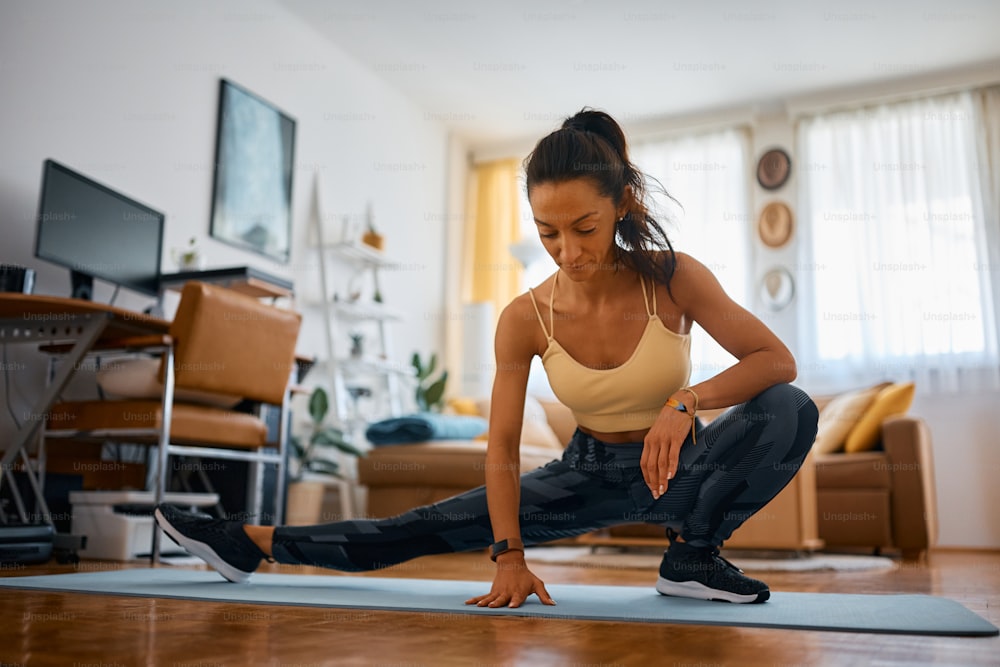 Athletic woman warming up and stretching her legs during home workout.