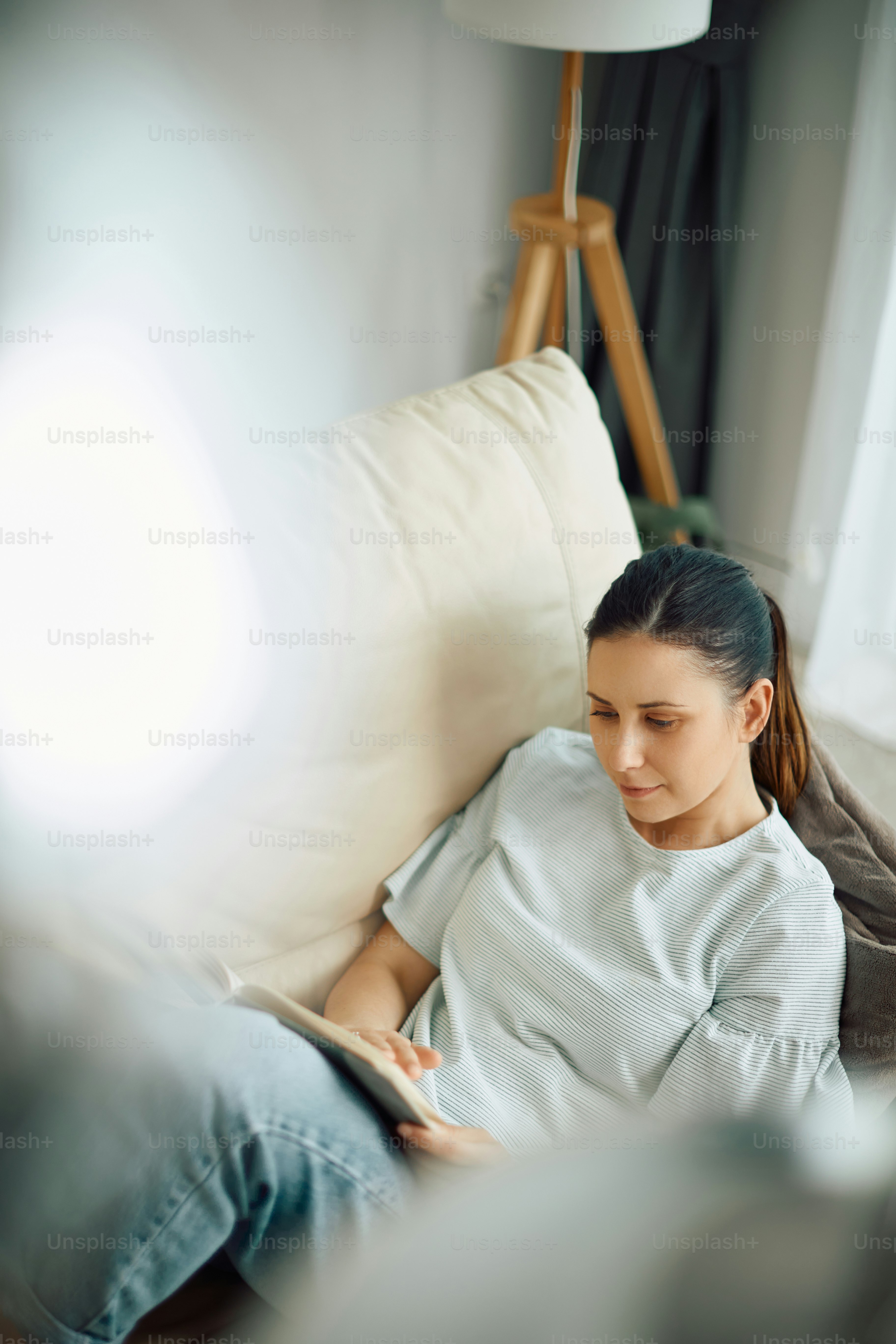 Mid adult woman enjoying in reading a book while relaxing on the sofa at home.