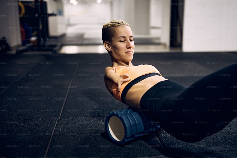 Mujer atlética con discapacidad usando un rodillo de espuma mientras calienta para el entrenamiento deportivo en un gimnasio.