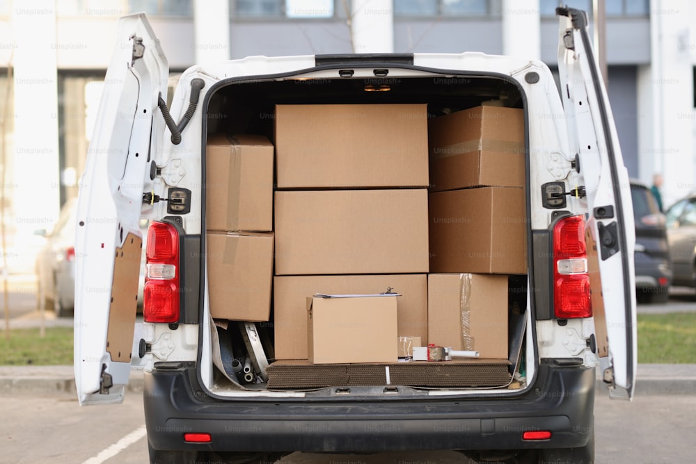 Many cardboard boxes lying in minibus with open door. Moving assistance cargo delivery concept