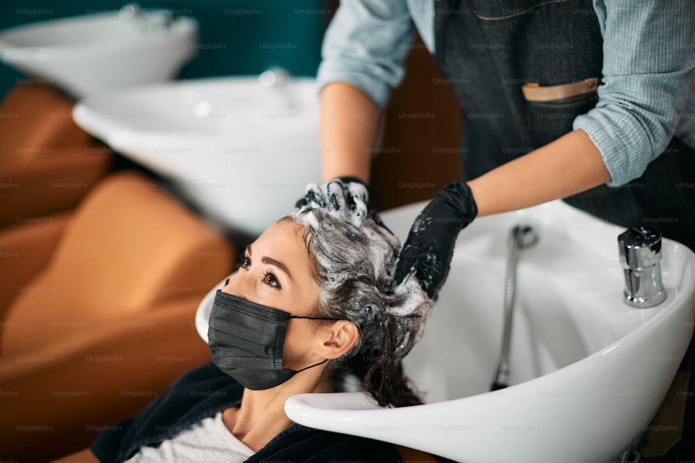 Junge Frau, die sich während der COVID-19-Pandemie im Salon die Haare waschen lässt.