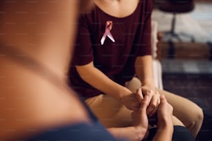 Gros plan d’une femme atteinte d’un cancer du sein et de son amie se tenant la main à la maison.