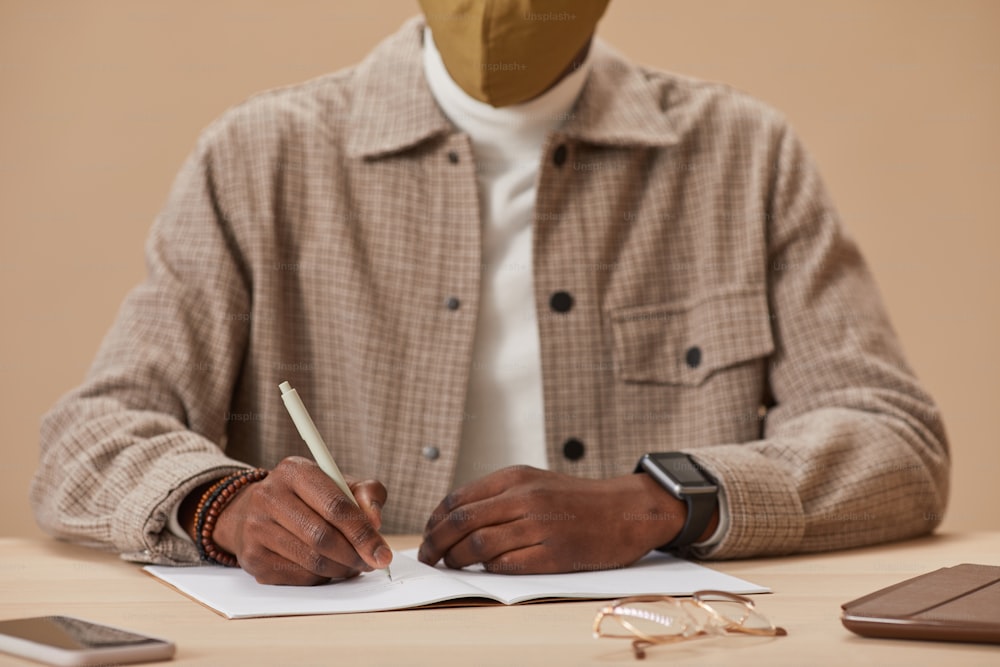Close-up of man sitting at the table making notes in notebook during online studying