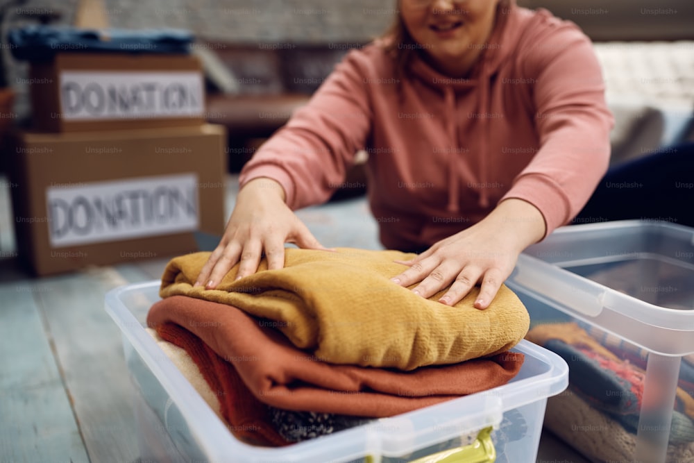 Close-up da mulher embalando a caixa de doação com roupas para pessoas necessitadas.