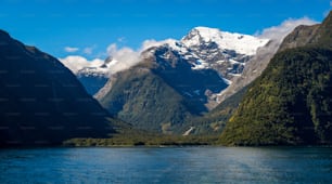 Lake and mountain landscape with snow capped peak under summer sunlight in blue sky background. Shot in Milford Sound, Fiordland National Park, South Island of New Zealand.