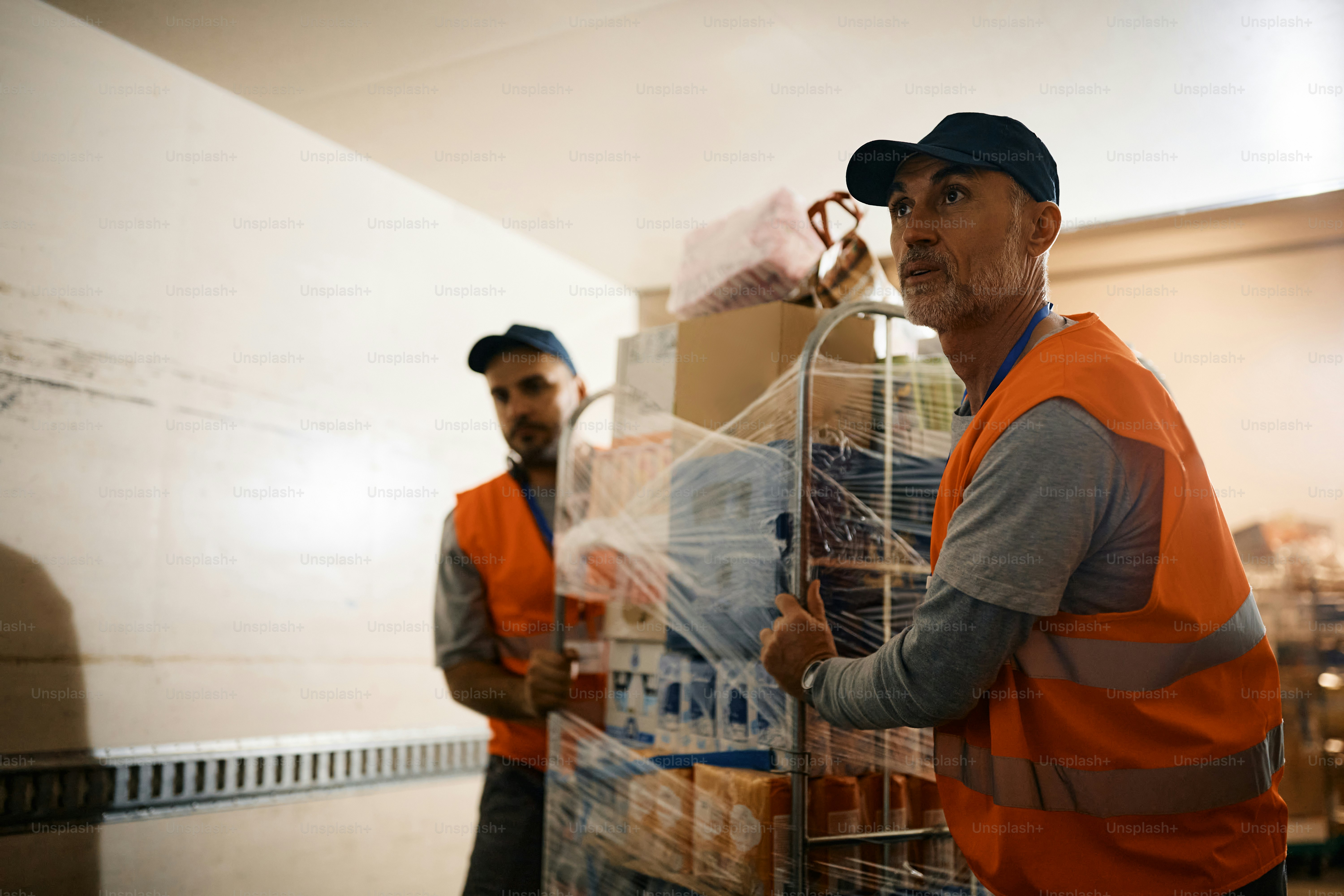 Reifer Lagerarbeiter mit Mitarbeiter, der Regal mit Paketen durch den Lagerflur bewegt. Speicherplatz kopieren.