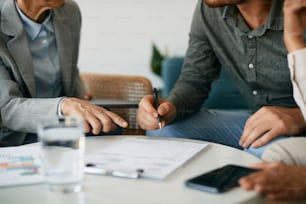 Close-up of couple closing a deal with their financial advisor and signing paperwork during the meeting.