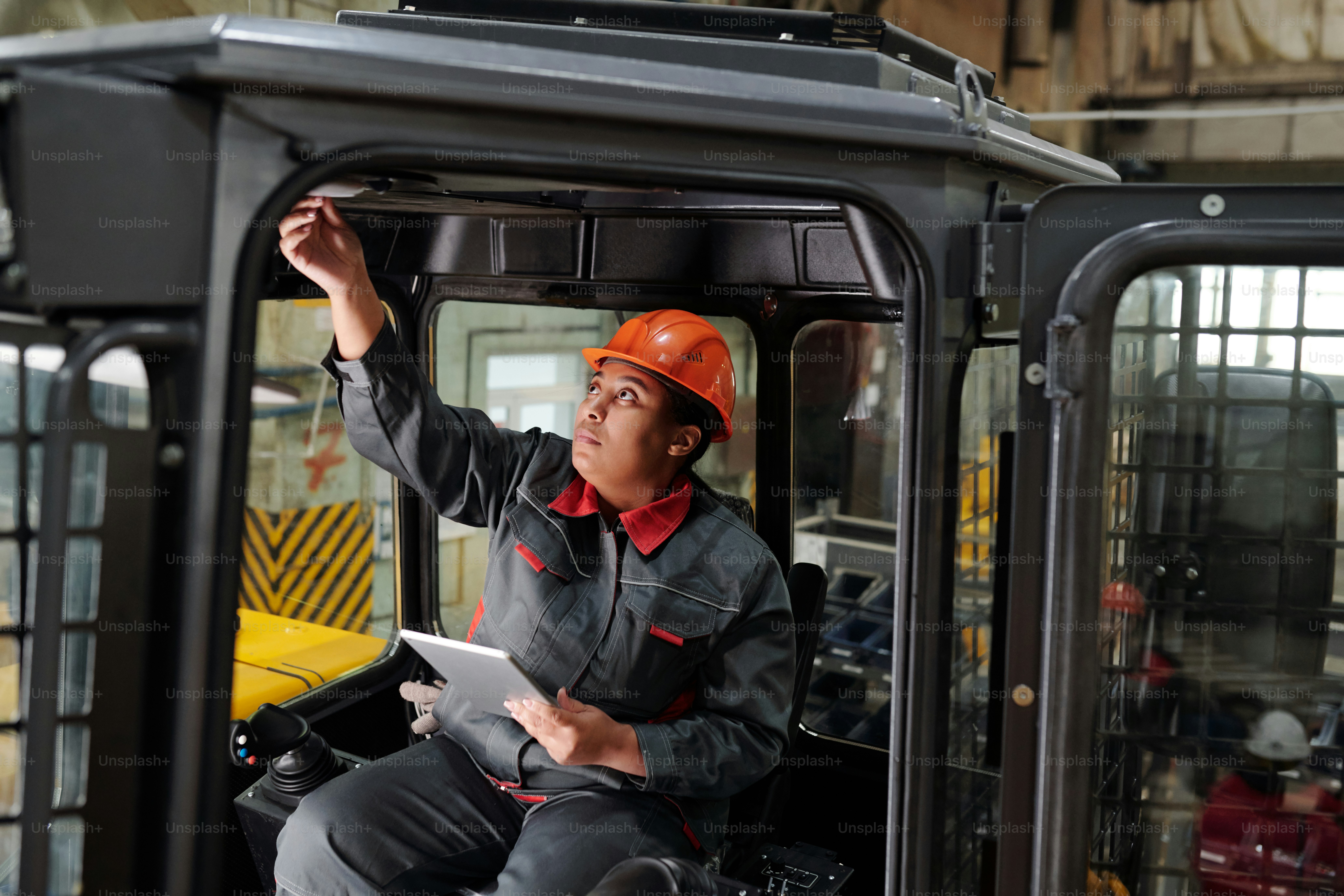 African American female worker of industrial plant with tablet driving construction machine while testing new vehicle