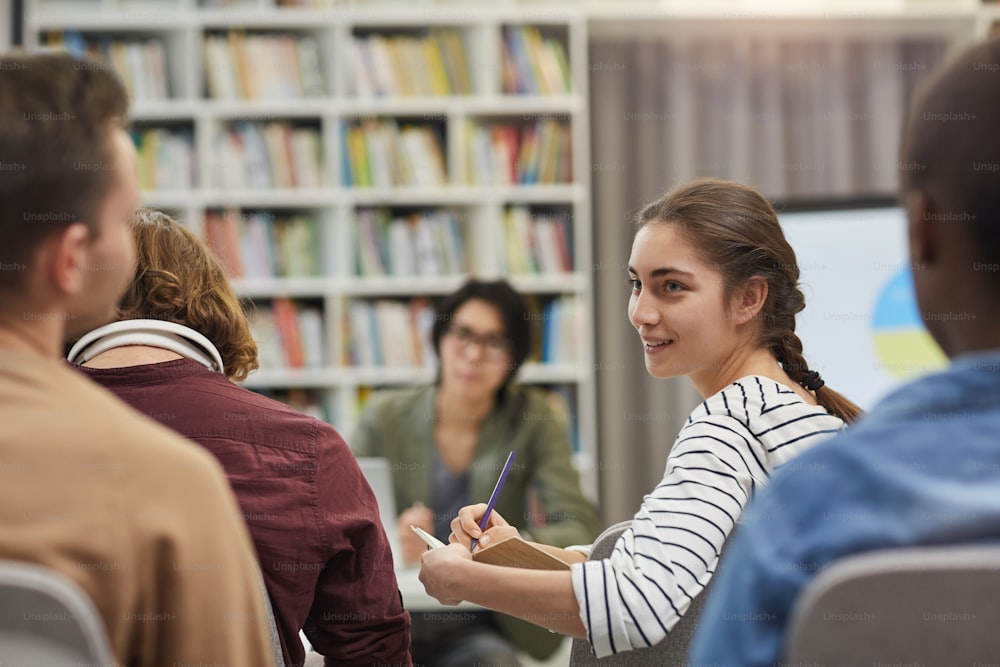 Moça fazendo anotações em seu caderno e discutindo com seus colegas durante a apresentação de negócios