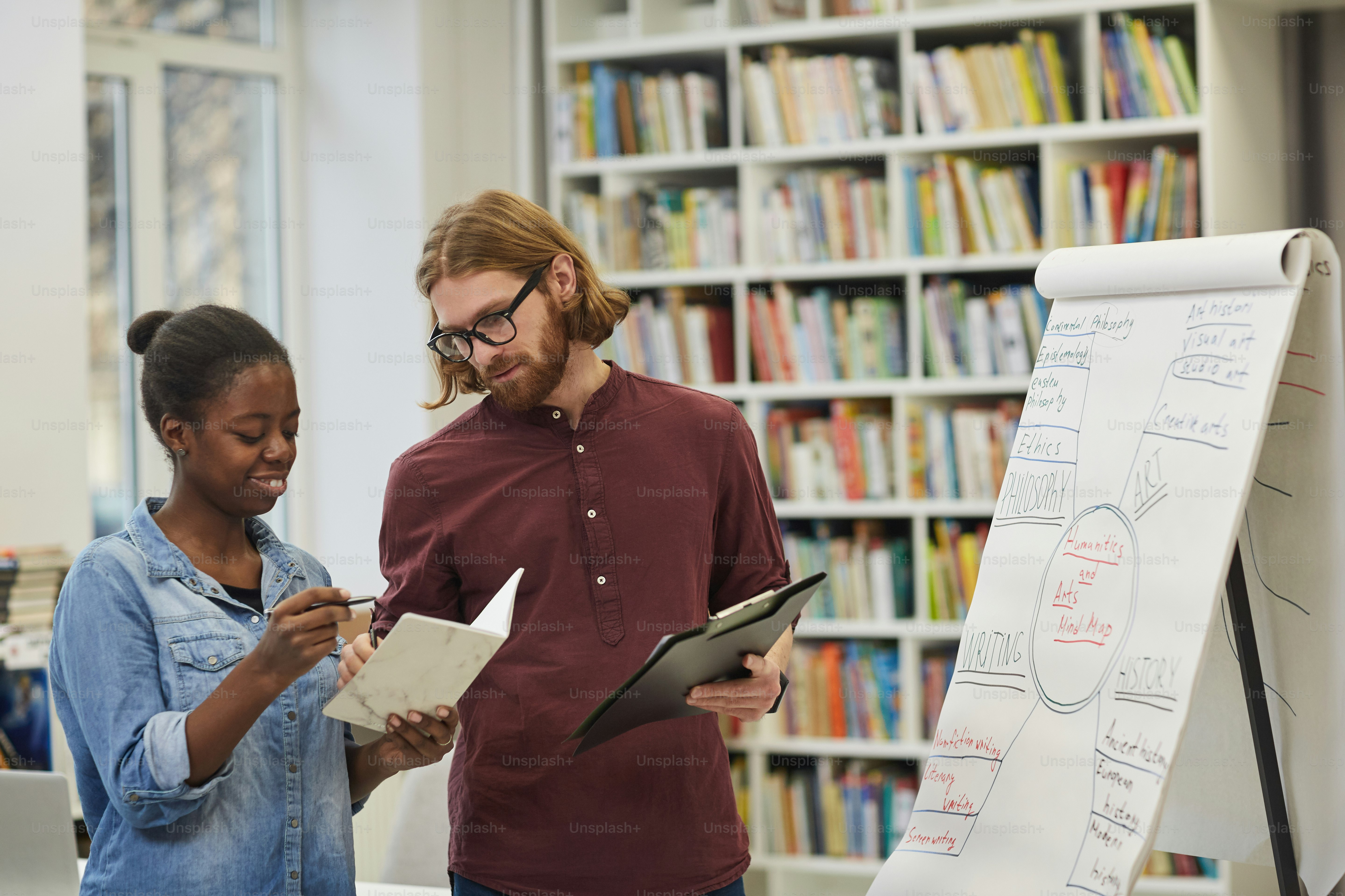 Young teacher explaining to African student the new material while they standing near the whiteboard after lecture