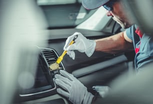 Automotive Cleaning and Detailing Business. Caucasian Worker Brushing Dirt Out From the Car Cockpit Elements.