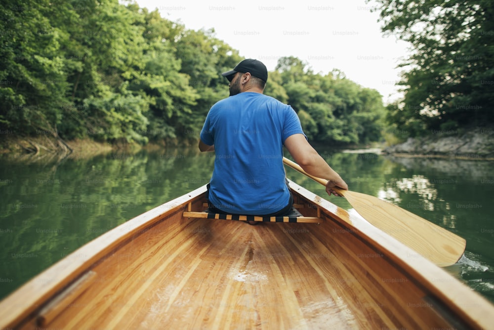 Rear view of man paddling canoe in the lake forest.