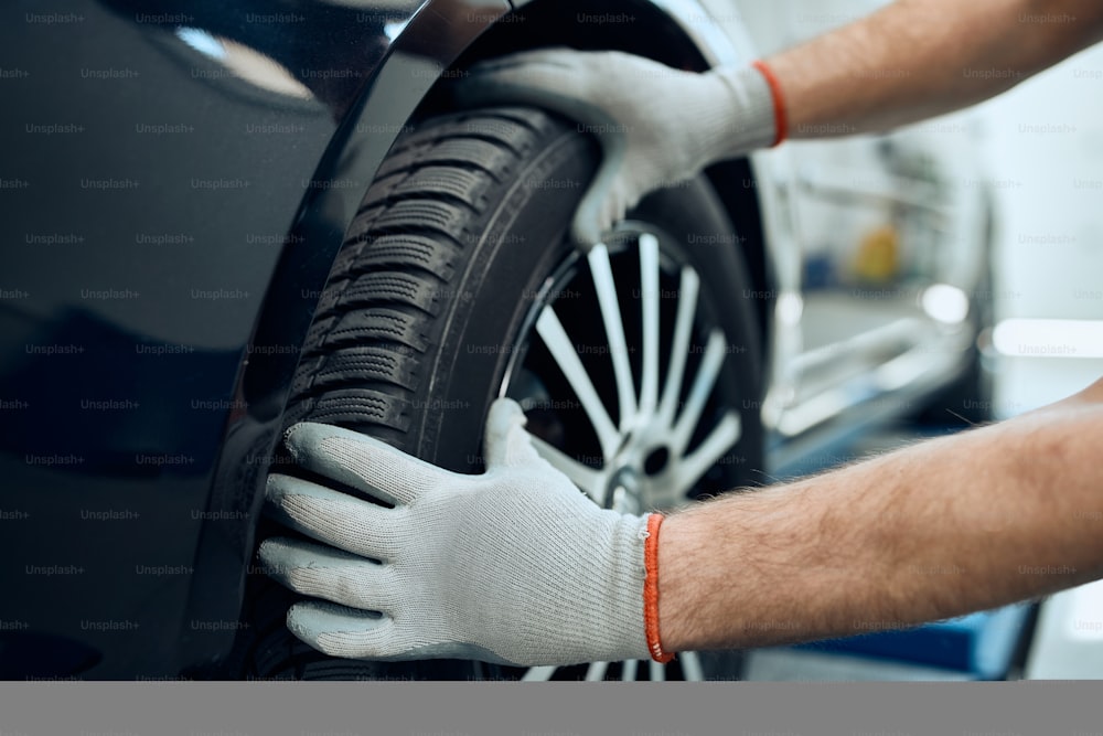 Gros plan d’un réparateur changeant un pneu de voiture à l’atelier de réparation automobile.