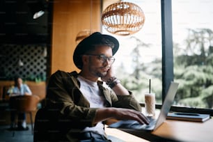 Young displeased man using laptop while surfing the net and e-learning in a cafe.