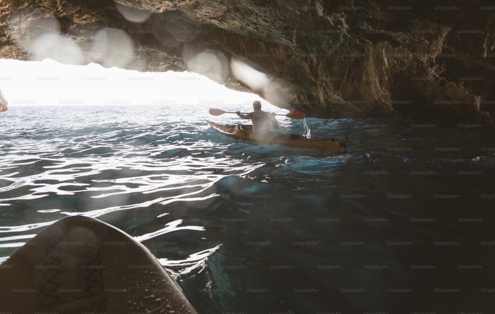 Vista trasera de un hombre remando en kayak en una cueva. Kayak y espeleología al mismo tiempo.