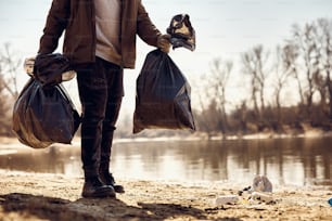 Uomo irriconoscibile che trasporta sacchi della spazzatura pieni dopo aver pulito la spiaggia. Copia spazio.