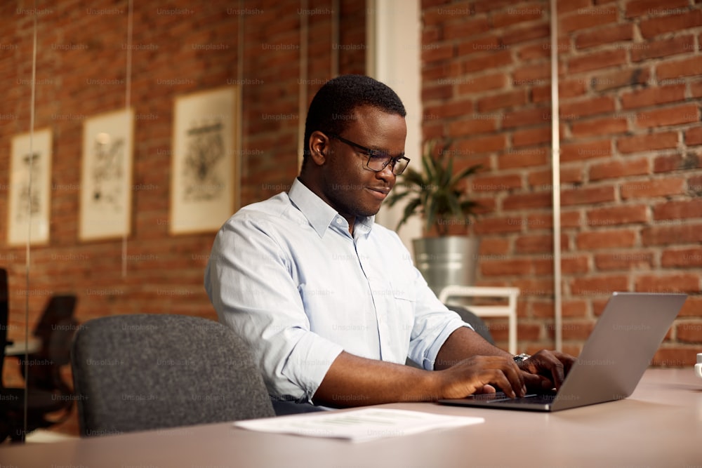 Hombre de negocios afroamericano usando una computadora portátil mientras trabaja en la oficina.