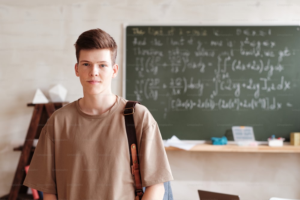 Portrait of schoolboy with backpack looking at camera while standing at empty classroom