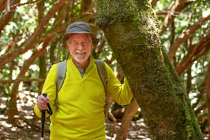 Lächelnder älterer Mann, der im Wald wandert und einen moosbedeckten Baumstamm berührt und einen gesunden Lebensstil genießt - Earth Day Konzept. Die Menschen müssen den Planeten vor der Abholzung retten