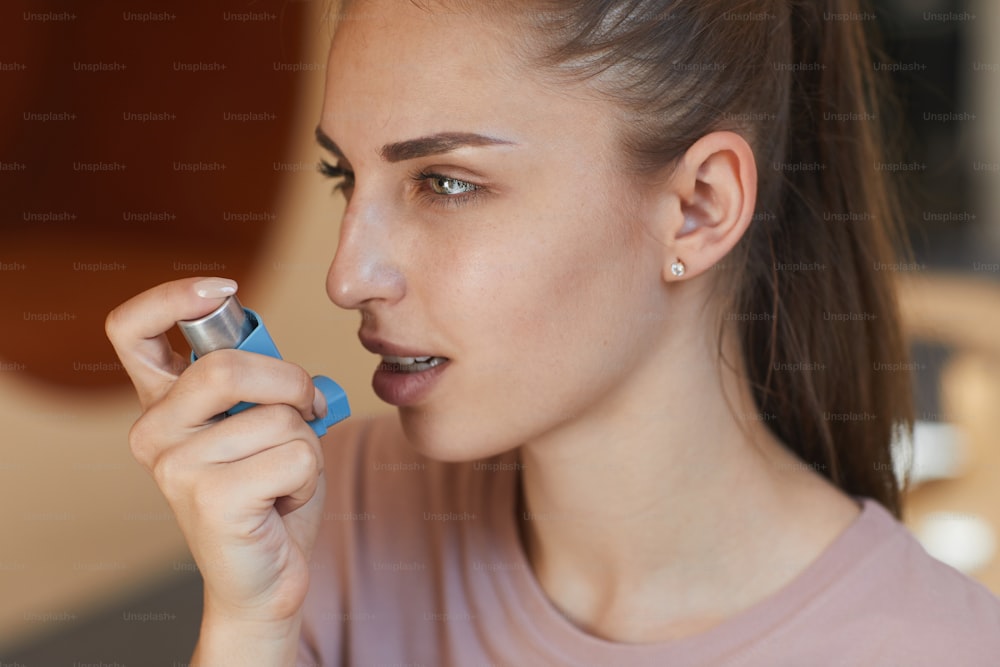 Close-up of attractive girl having breath problem using asthma inhaler to breathe medicine into lungs