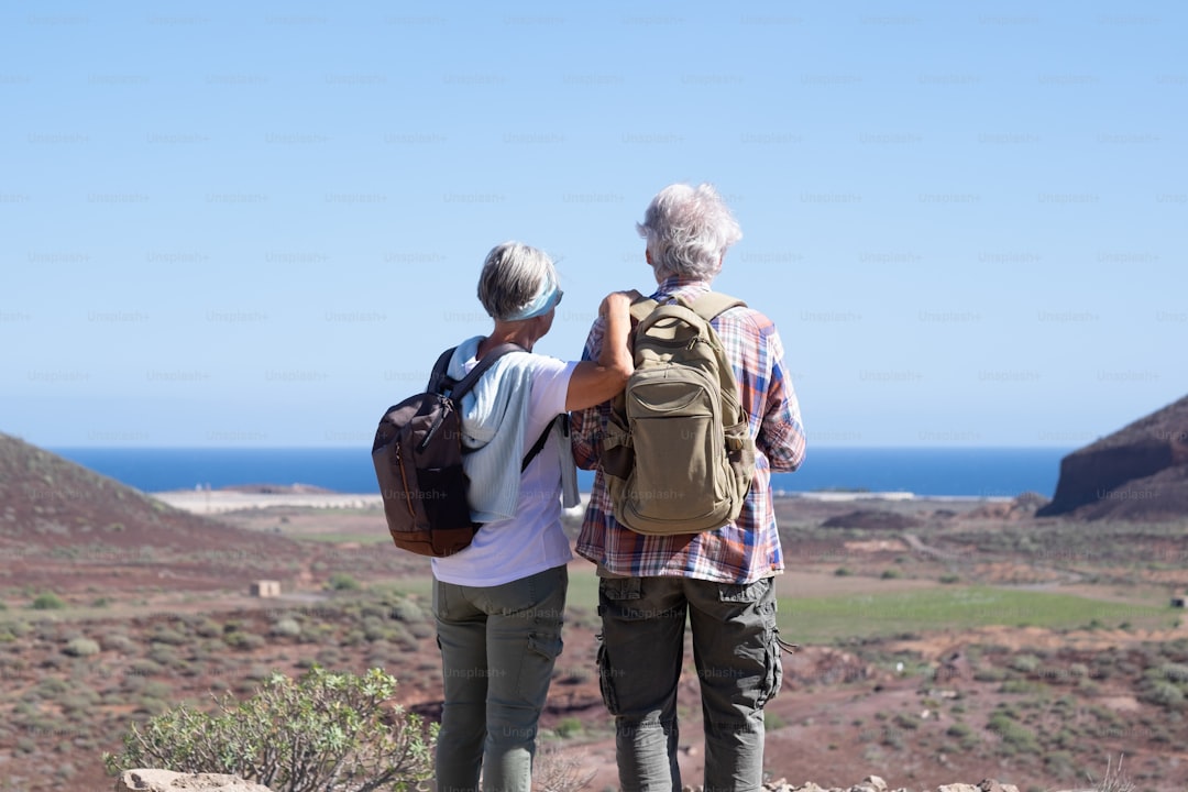 Active senior couple with backpacks in outdoors excursion hiking in mountain looking at horizon enjoying healthy lifesty