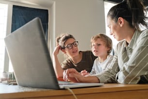 Two lesbian mothers talking to their son while sitting at table in front of laptop during online lesson