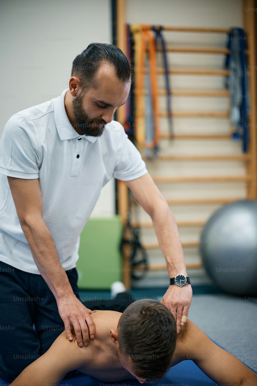 Fisioterapeuta dando massagem nos ombros para o homem atlético durante o tratamento de reabilitação no clube de saúde.