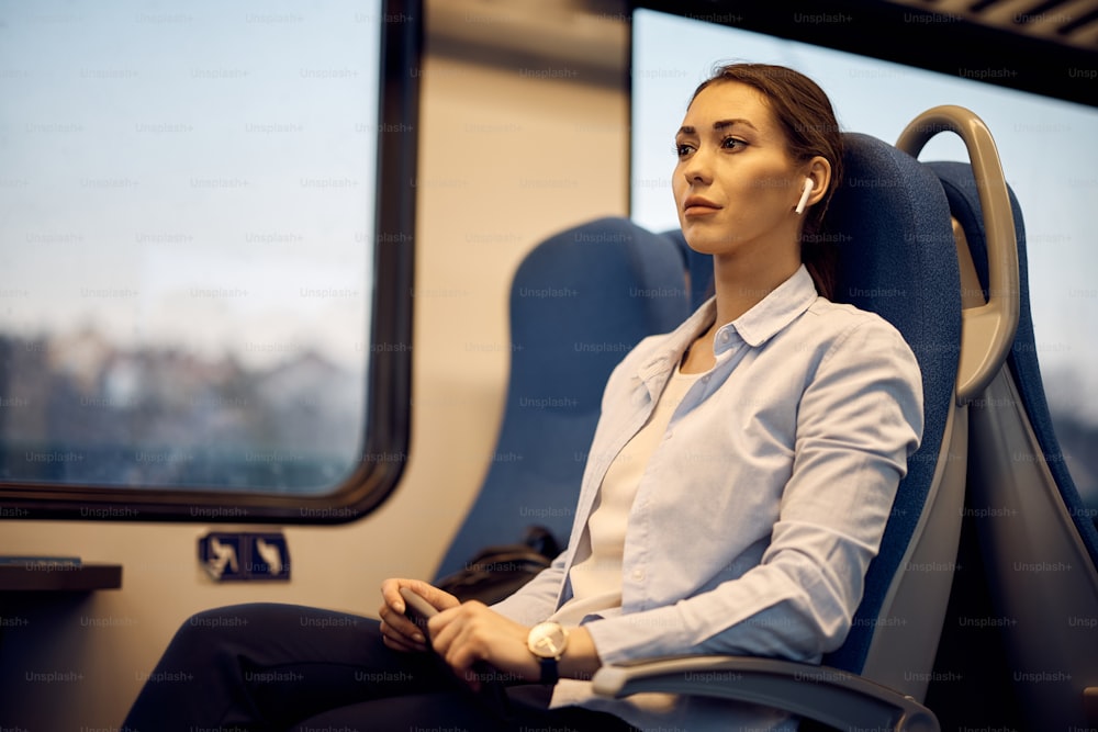 Junge Frau träumt und hört Musik über Ohrhörer, während sie mit dem Zug pendelt.
