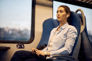 Giovane donna che sogna ad occhi aperti e ascolta musica sugli auricolari mentre si sposta in treno.