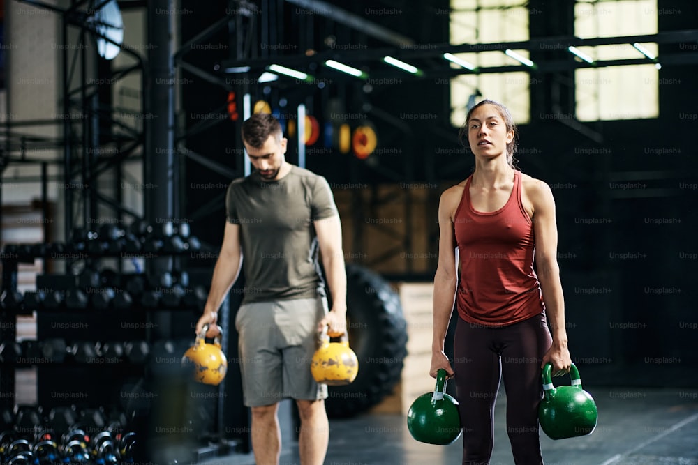Mulher atlética e seu amigo do sexo masculino se exercitando com kettlebells durante o treinamento esportivo em uma academia.