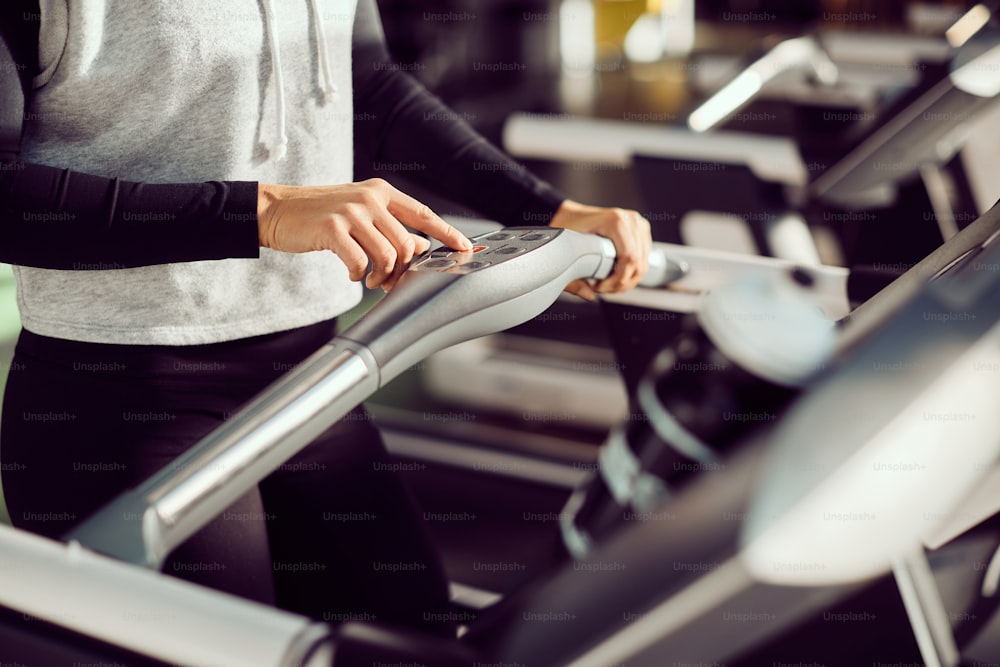 Close-up of athletic woman pressing start button while exercising on treadmill at health club.