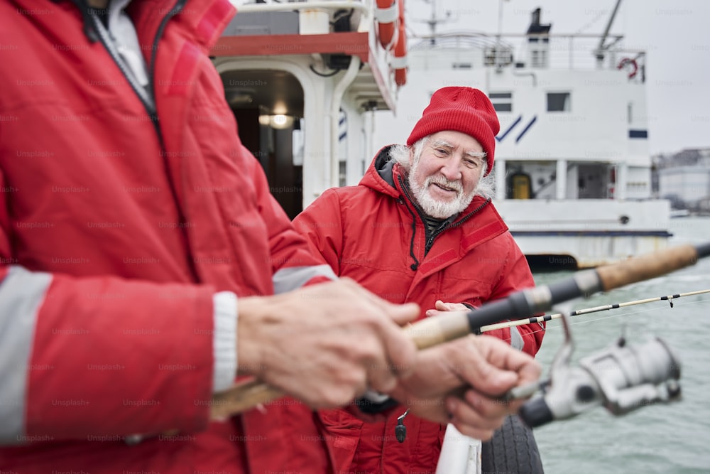 Professional fishing. Waist up portrait view of the senior bearded man telling something to his young colleague while preparing to the fishing. Stock photo